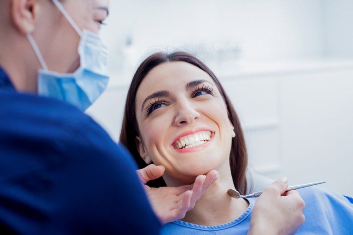 A smiling woman in a dental chair with a dentist wearing a mask and examining her teeth.
